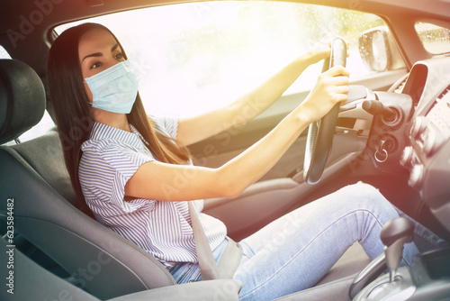Beautiful young woman in safety mask sitting in a car, protective mask against coronavirus, driver on a city during a coronavirus outbreak. Business trips during pandemic