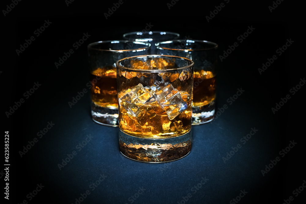 Four glasses of bourbon whiskey with ice cubes stand in a spot of light against a black background Four glasses of bourbon whiskey with ice cubes stand in a spot of light against a black background