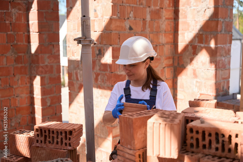 Tableau sur toile Woman bricklayer in hardhat and building uniform sorting bricks