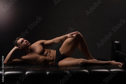 Young muscle man in underwear lying on sofa in dark room