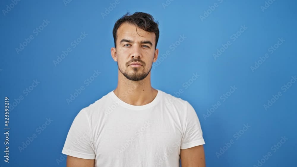 Young hispanic man standing with serious expression over isolated blue background Young hispanic man standing with serious expression over isolated blue background