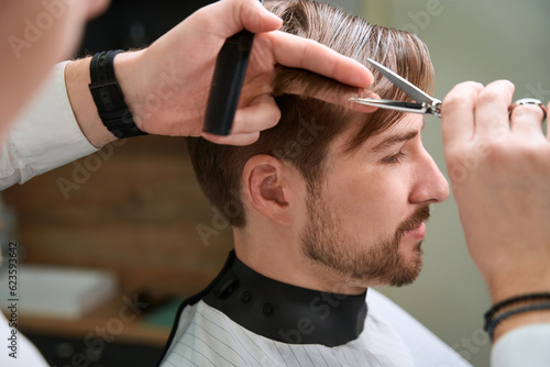 Handsome man receiving services from barber in modern barbershop