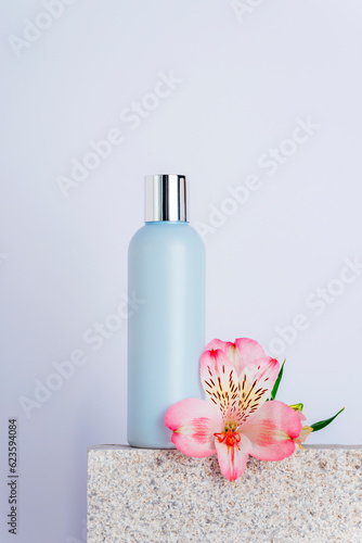 Cosmetic facial cleanser bottle and alstroemeria pink flower on natural stone podium, closeup