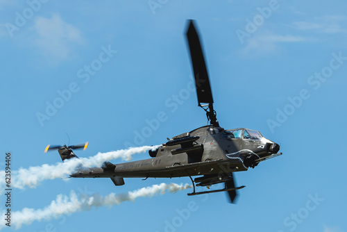 Cobra attack helicopter in flight against blue sky with smoke trailing from pods