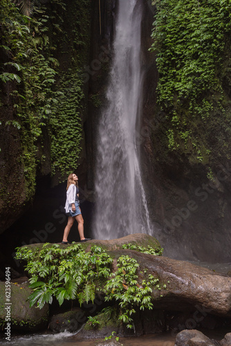 Waterfall in tropical jungle and alone woman tourist. Leke Leke waterfall in Bali, Indonesia.