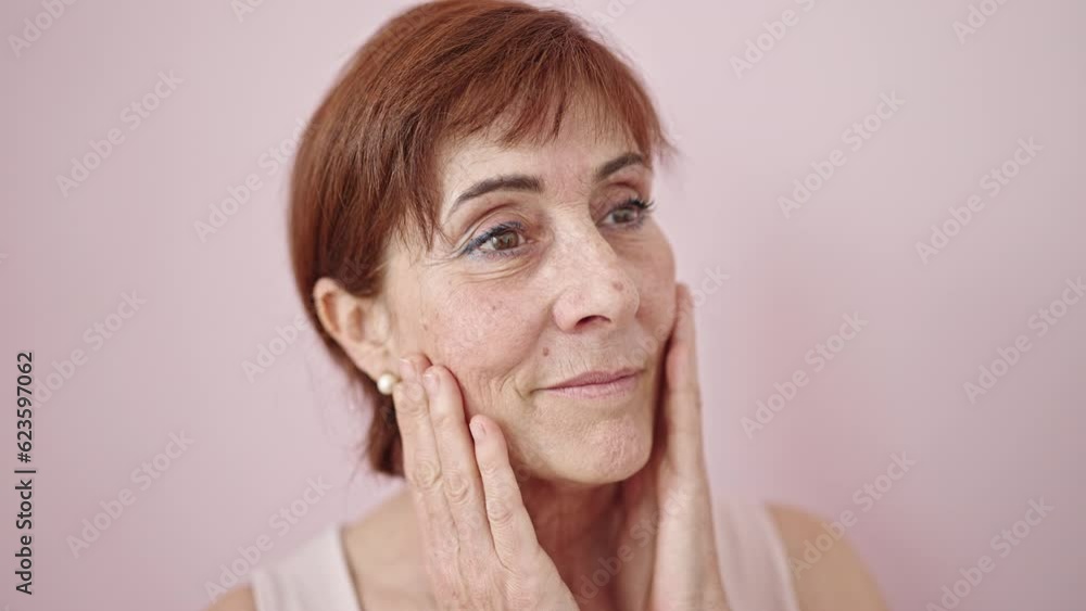 Mature hispanic woman looking serious touching face with hand over isolated pink background Mature hispanic woman looking serious touching face with hand over isolated pink background