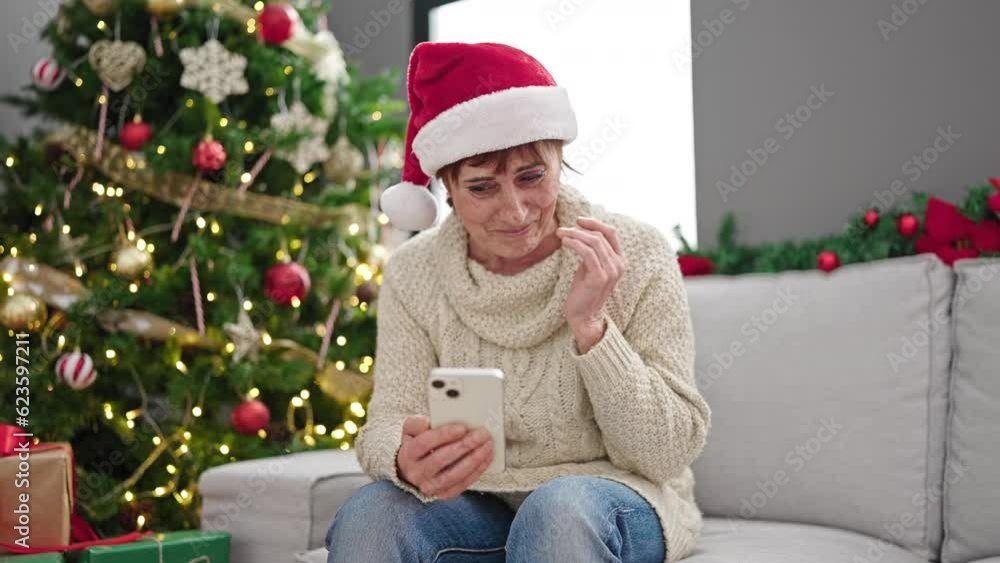 Mature hispanic woman using smartphone sitting by christmas tree at home Mature hispanic woman using smartphone sitting by christmas tree at home