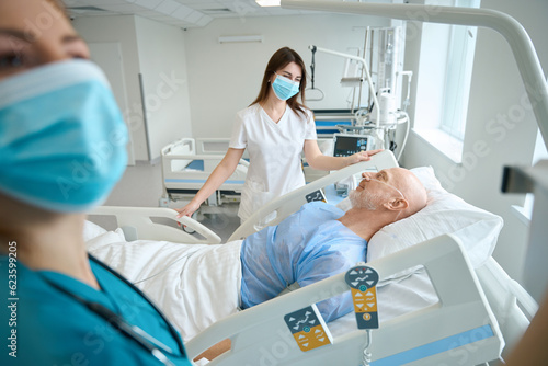 Therapists customizing medical equipment near patient on bed in chamber