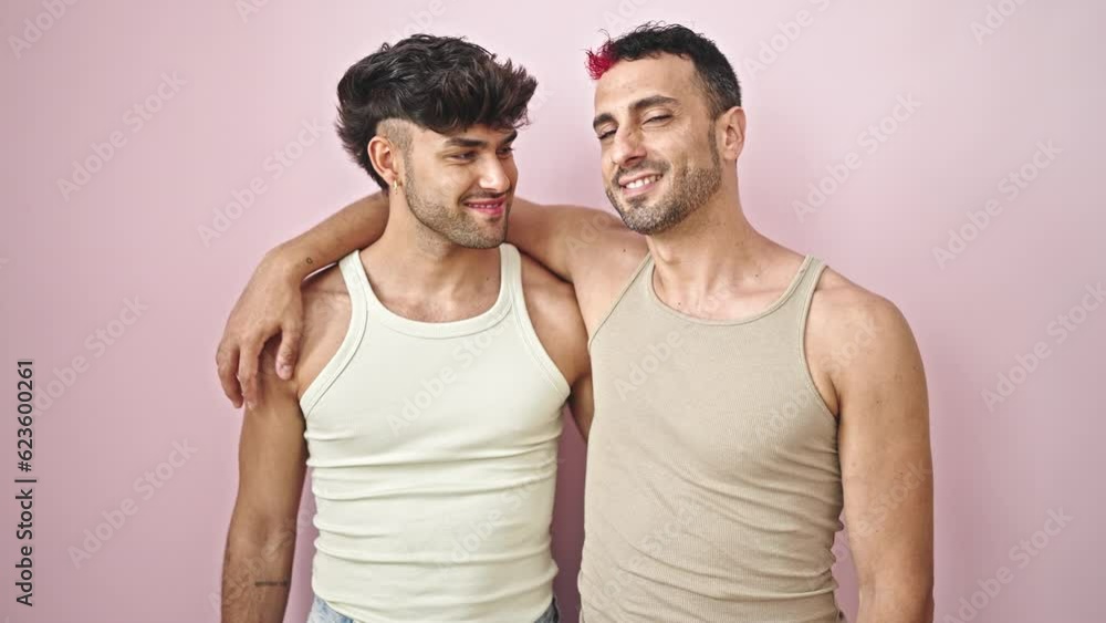 Two men couple smiling confident hugging each other over isolated pink background Two men couple smiling confident hugging each other over isolated pink background