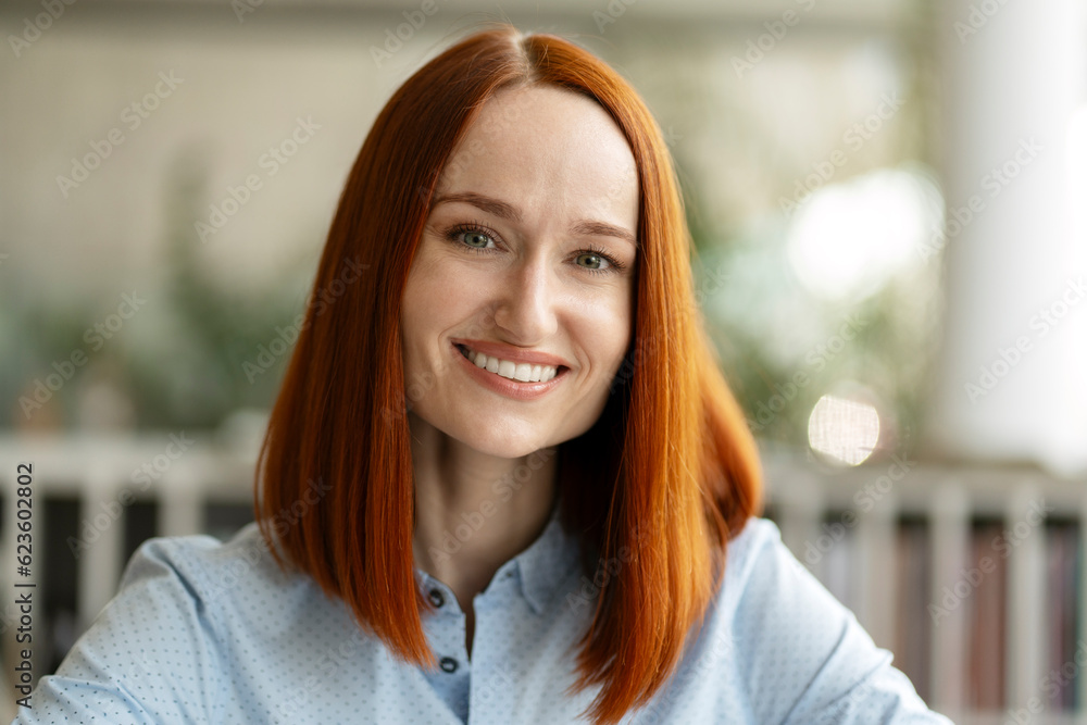 Fototapeta premium Closeup portrait of beautiful smiling red haired student standing in university campus, education concept. Confident businesswoman, successful manager looking at camera sitting in modern office 