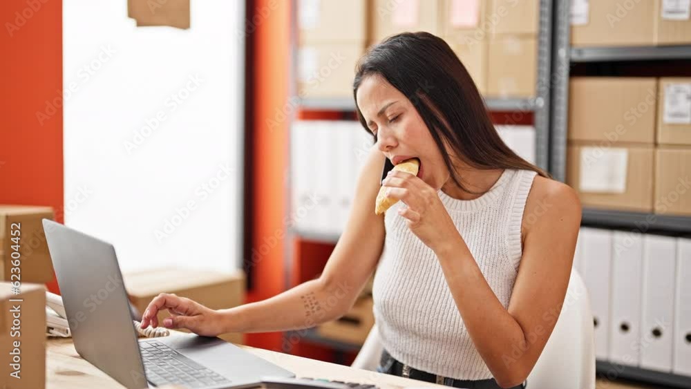 Young beautiful hispanic woman ecommerce business worker eating croissant working at office Young beautiful hispanic woman ecommerce business worker eating croissant working at office