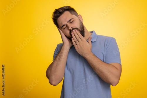 Tired overworked young caucasian man yawning, sleepy inattentive feeling somnolent lazy bored gaping suffering from lack of sleep. Handsome exhausted guy isolated on studio yellow background indoor