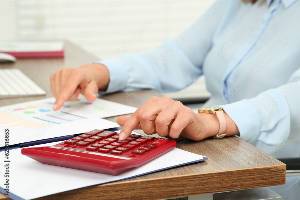 Accountant using calculator at wooden desk in office, closeup Accountant using calculator at wooden desk in office, closeup