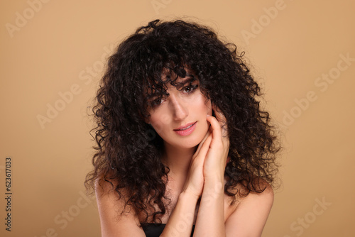 Beautiful young woman with long curly hair on beige background