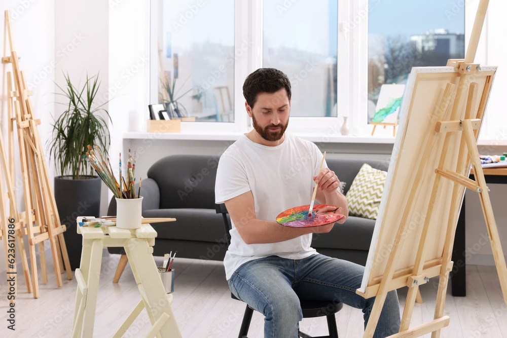 Man painting in studio. Using easel to hold canvas Man painting in studio. Using easel to hold canvas