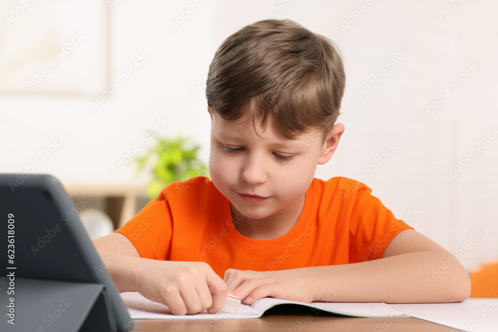 Little boy erasing mistake in his notebook at wooden desk indoors Little boy erasing mistake in his notebook at wooden desk indoors