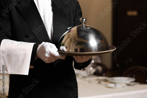 Butler holding metal tray with lid in restaurant, closeup