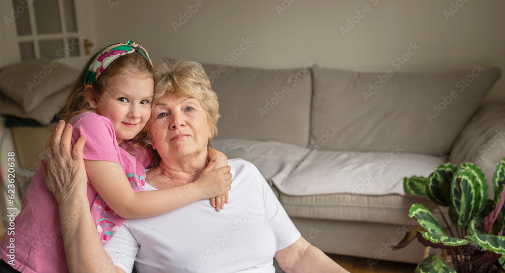 Grandmother hugging grand kid on couch at home, holding little girl in arms. senior grandma enjoying leisure time with cute granddaughter, talking to child. Family relations