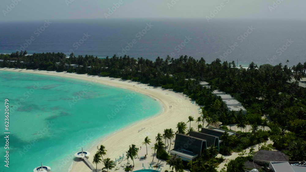 Aerial view of luxury villas over water on blue lagoon, white sandy beach. An island with bungalows over water standing in rows in the Maldives.