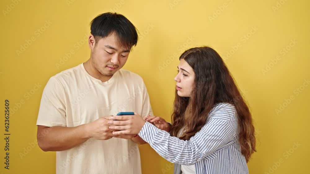 Man and woman couple using smartphone asking for attention over isolated yellow background Man and woman couple using smartphone asking for attention over isolated yellow background