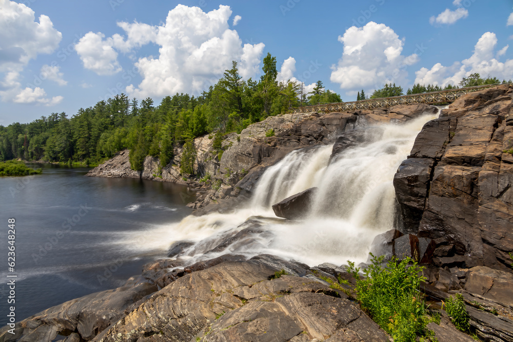 Fototapeta premium High Falls in the Muskoka town of Bracebridge, Ontario flows into the lake below on a bright sunny day.