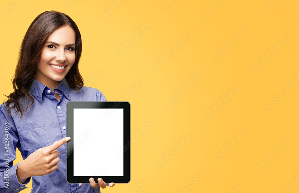 Happy smiling brunette businesswoman showing blank tablet pc monitor, with copy space area for some text, advertising or slogan, isolated over orange yellow color background. Business woman at studio. Happy smiling brunette businesswoman showing blank tablet pc monitor, with copy space area for some text, advertising or slogan, isolated over orange yellow color background. Business woman at studio.