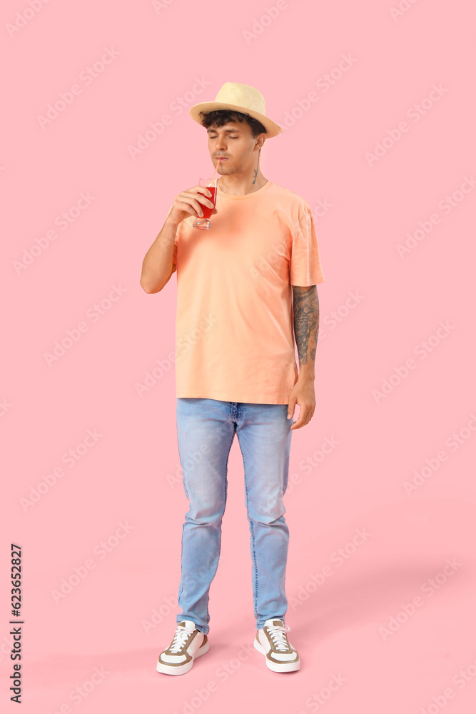 Young man drinking red juice on pink background Young man drinking red juice on pink background