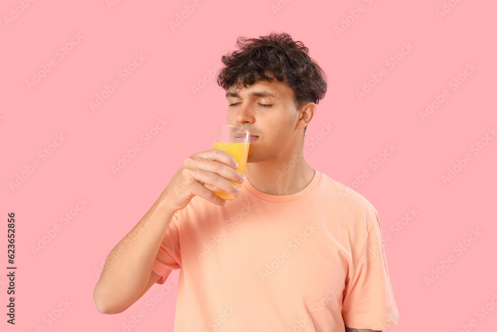 Young man with glass of orange juice on pink background Young man with glass of orange juice on pink background