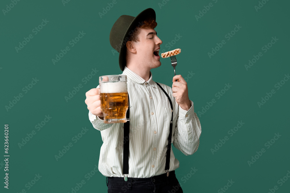 Young man in traditional German clothes with beer eating sausage on green background Young man in traditional German clothes with beer eating sausage on green background