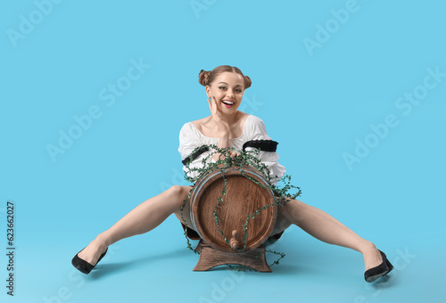 Beautiful Octoberfest waitress with barrel of beer sitting on blue background