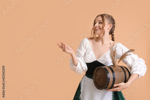 Beautiful Octoberfest waitress with barrel of beer showing something on beige background