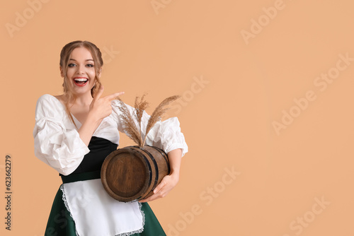 Beautiful Octoberfest waitress with barrel of beer on beige background