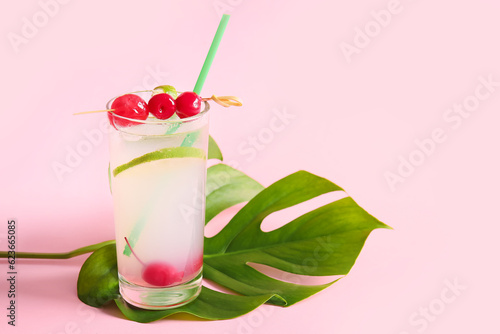 Glass of tasty cocktail with maraschino cherries on pink background