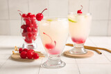 Glasses of tasty cocktail with maraschino cherries on white tile background