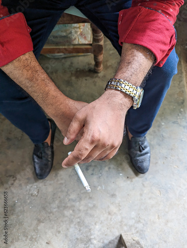 A smoker sitting with an ignited cigarette top section close-up shot. Portrait of a smoker's hand holding a cigarette. Unhealthy lifestyle concept with a cigarette on a blurry background.