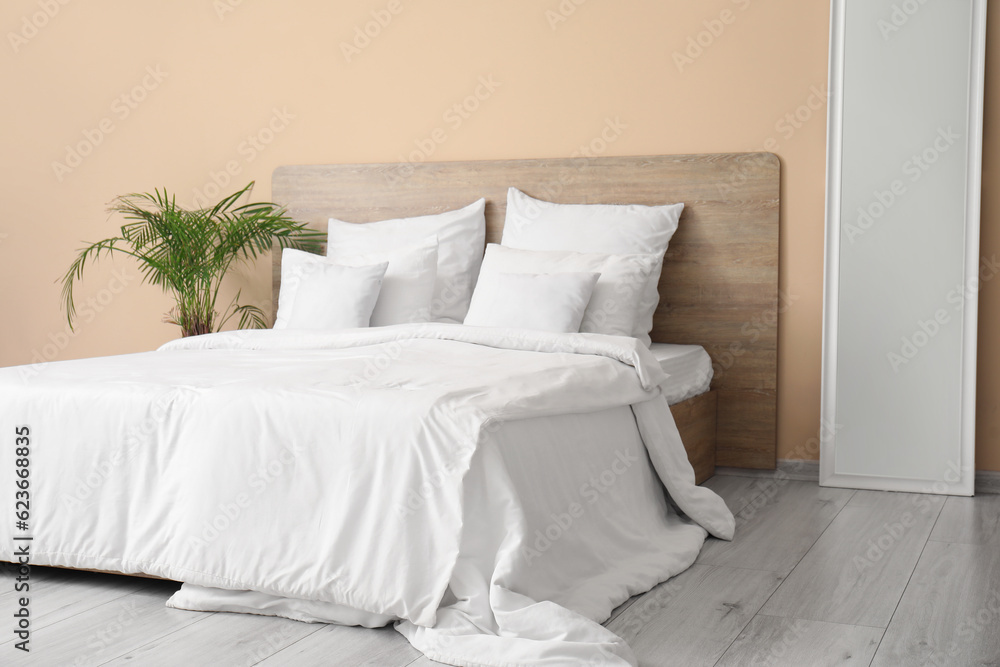 Obraz premium Comfortable bed with white pillows, mirror and houseplant in bedroom