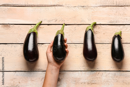 Woman with fresh eggplants on light wooden background