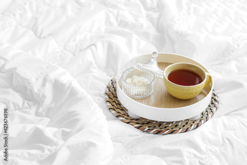 Tray with cup of tea on white blanket in bed, closeup