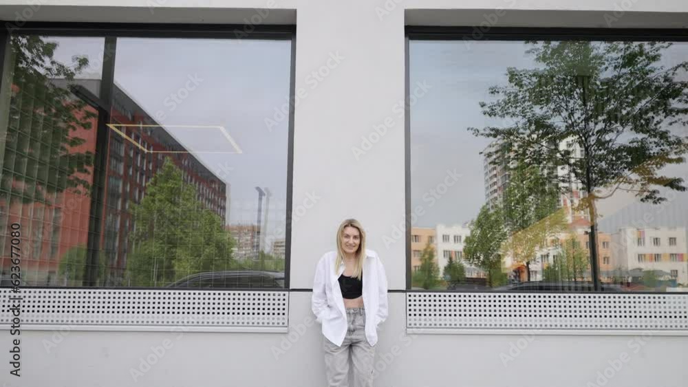 Summer mood. A girl with blonde hair looks at the camera. Happy girl in the camera. The white wall and trees reflected in the windows of the building. Summer mood. A girl with blonde hair looks at the camera. Happy girl in the camera. The white wall and trees reflected in the windows of the building.