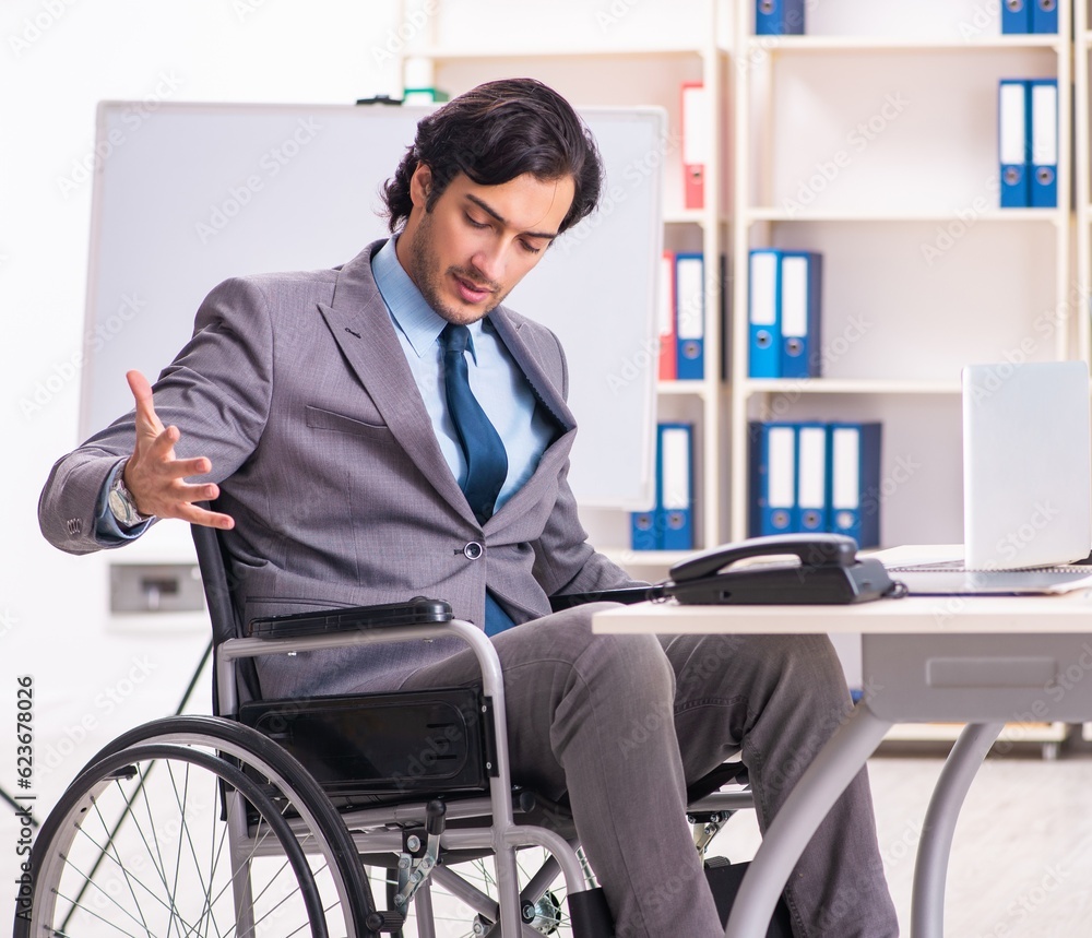Young handsome employee in wheelchair at the office Young handsome employee in wheelchair at the office