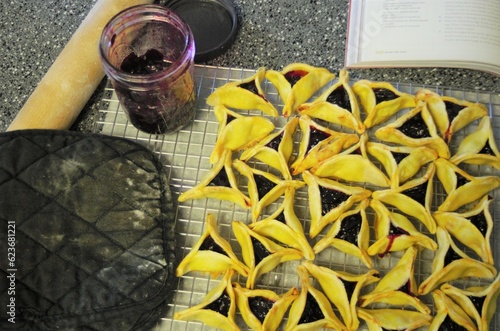 Top down view of cooked jelly-filled pastries, with oven mitt, rolling pin, jar of cherry jam and a cookbook.Taken while making Hamantaschen, a traditional Ashkenazi Jewish  triangularly shaped pastry photo