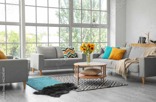 Fotografia Cozy grey sofas and vase with beautiful sunflowers in interior of light living r