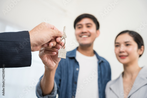 Focus on keys. Happy asian couple is taking keys from their new house from broker and smiling. Hands of estate agent giving keys to the couple. The agent handed the keys a young couple.