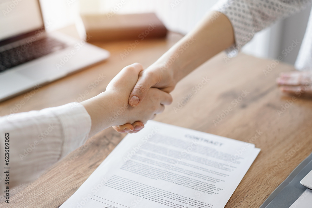 Obraz premium Business people shaking hands above contract papers just signed on the wooden table, close up. Lawyers at meeting. Teamwork, partnership, success concept