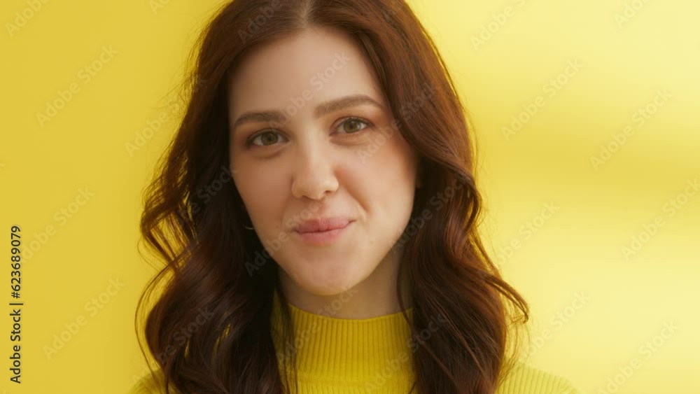 Medium shot of cutie in yellow sweater on yellow background, flirting at camera. Young brunette smiles, looks down and straight at camera, biting lips. High quality 4k footage Medium shot of cutie in yellow sweater on yellow background, flirting at camera. Young brunette smiles, looks down and straight at camera, biting lips. High quality 4k footage