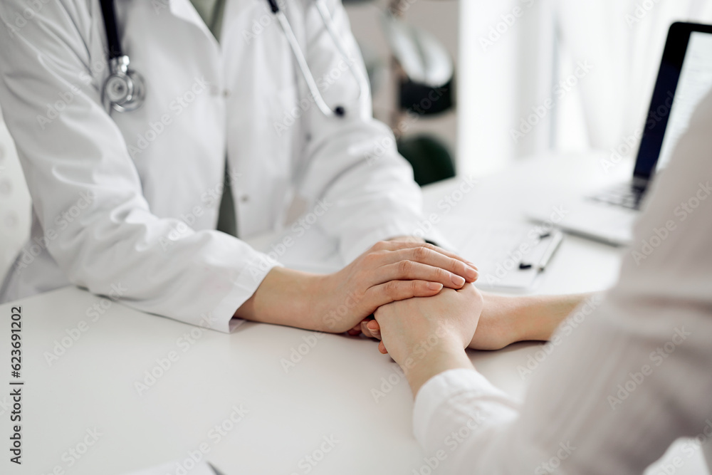 Doctor and patient sitting at the white table near window in clinic. Female physician's hands reassuring woman. Medicine concept Doctor and patient sitting at the white table near window in clinic. Female physician's hands reassuring woman. Medicine concept