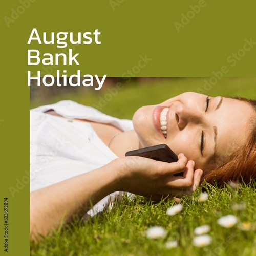 August bank holiday text on green with happy caucasian woman lying on grass in sun on smartphone