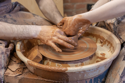 potter teaches the child. A craftsman sits on a bench with a potter's wheel and makes a clay pot. National craft. Hands close-up