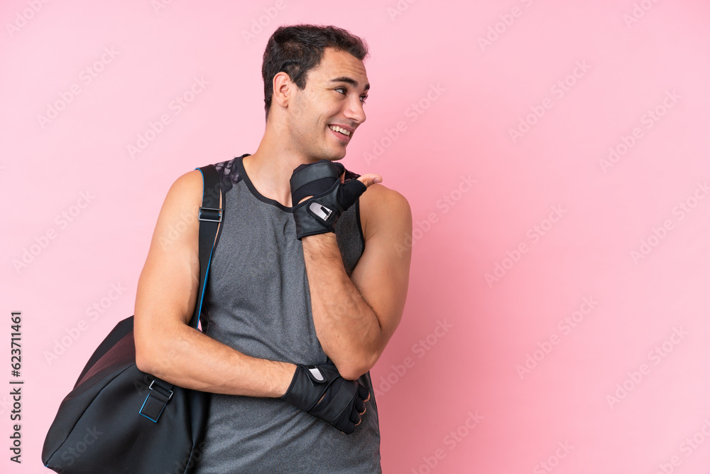 Young sport caucasian man with sport bag isolated on pink background pointing to the side to present a product
