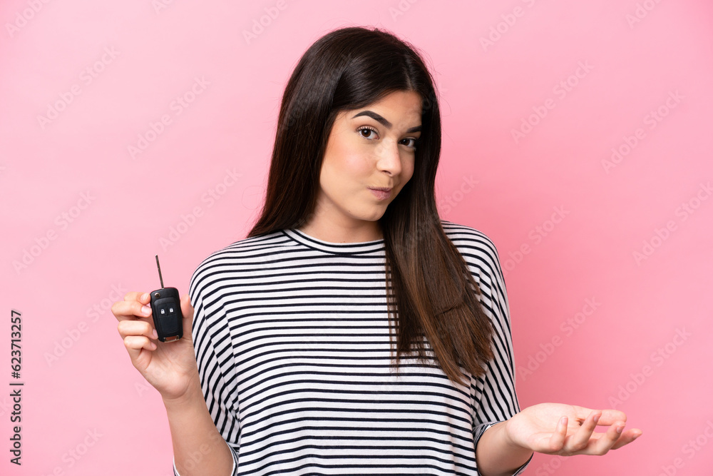 Young Brazilian woman holding car keys isolated on pink background making doubts gesture while lifting the shoulders Young Brazilian woman holding car keys isolated on pink background making doubts gesture while lifting the shoulders